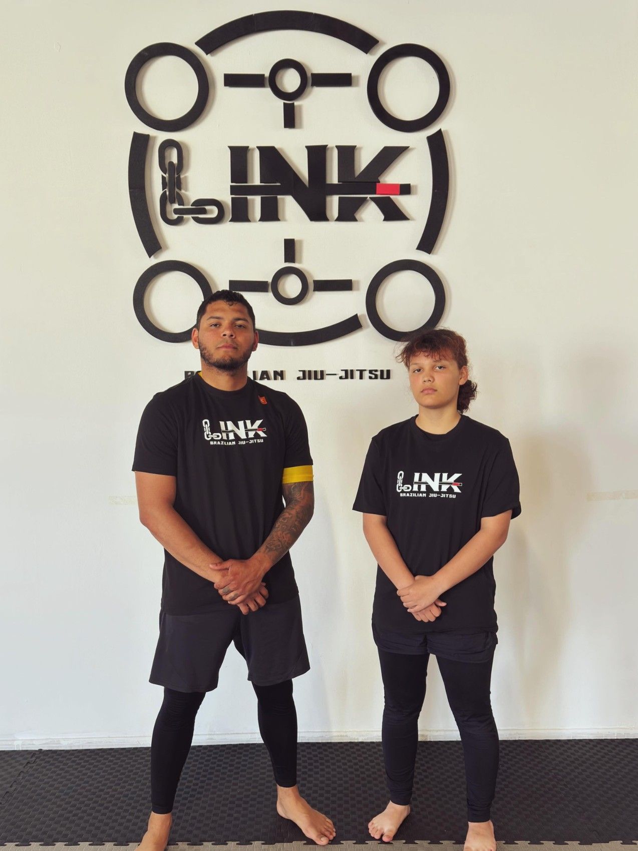 Dos alumnos con camiseta de LINK frente al logo de la academia
