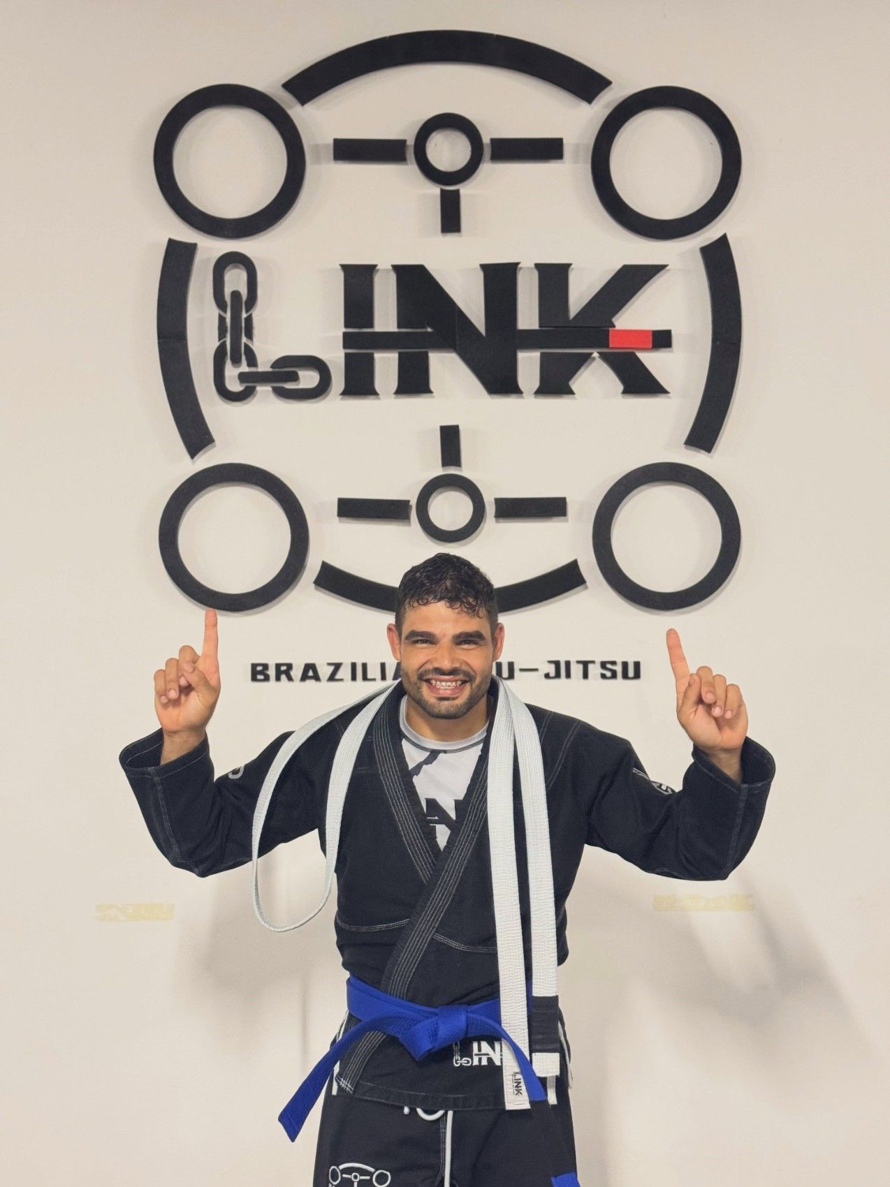 Alumno con su nuevo cinturón azul señalando el logo de LINK