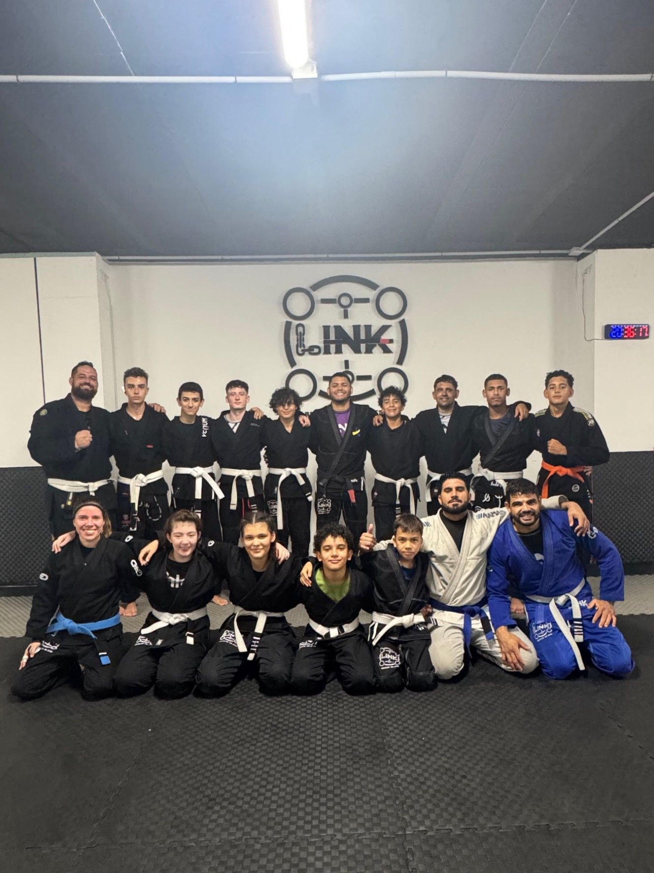 Alumnos de LINK Brazilian Jiu-Jitsu con kimono, adultos y niños, junto al profesor bajo el logo de la academia en Torrevieja