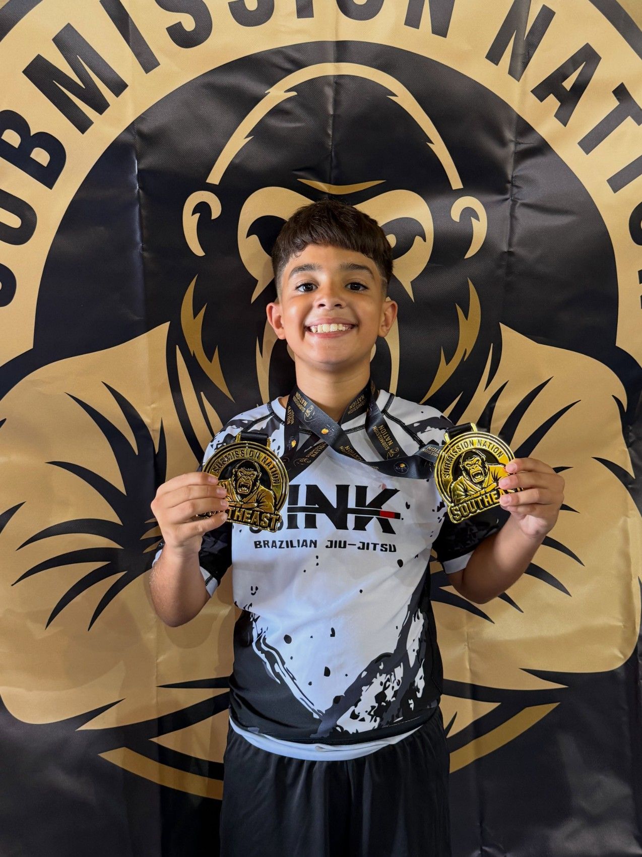 Peque de LINK sonriendo con dos medallas de oro y el rashguard de la academia